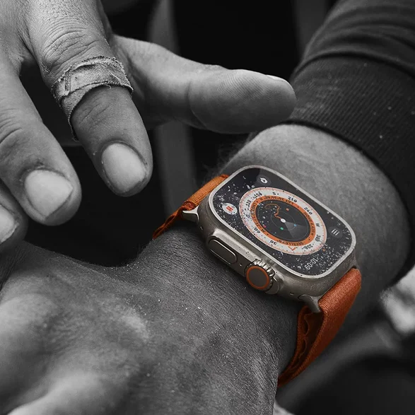 Nahaufnahme der Apple Watch Ultra mit orangenem Alpine Loop am Handgelenk eines Wanderers mit offener Kompass-App