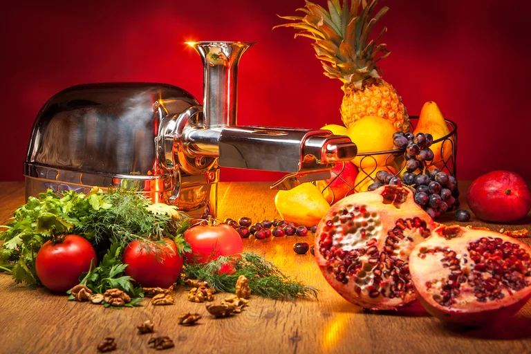 Chrom Slow Juicer mit Obst auf Holzplatte und rotem Hintergrund