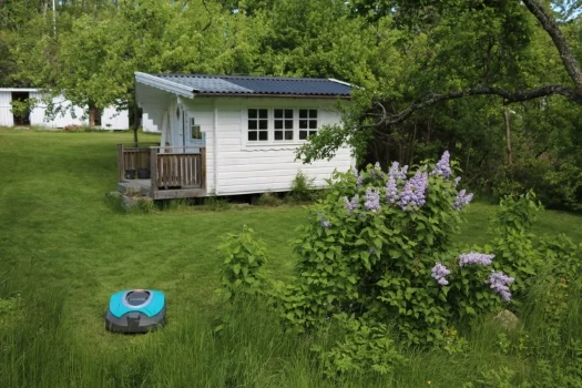 Gartenhütte im Grünen, um die ein Mähroboter fährt