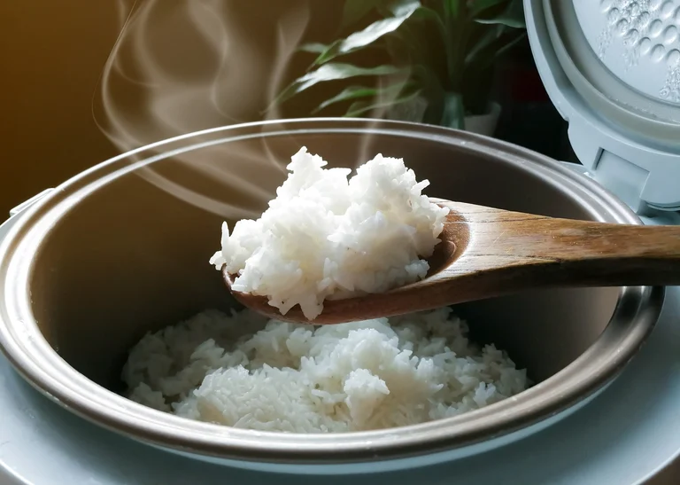 Reiskocher mit Reislöffel und dampfendem gekochtem Reis.