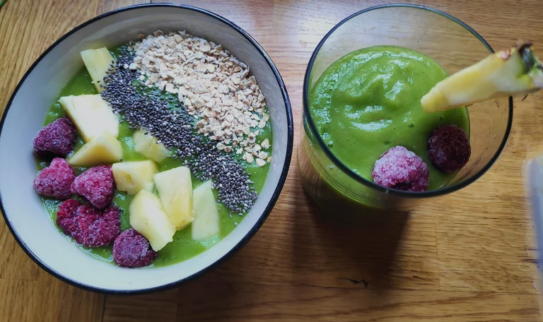 Smoothie Bowl und Glas mit grünem Smoothie auf Holz