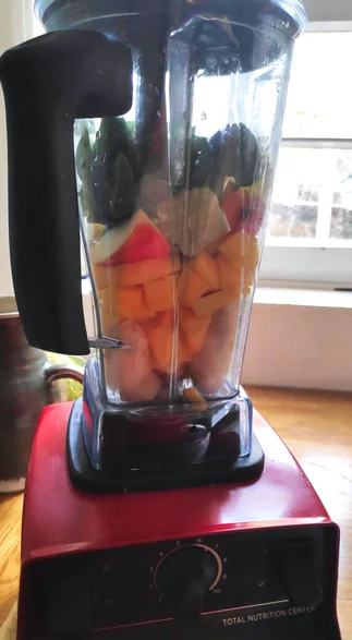 Roter Hochleistungsmixer von Vitamix mit Zutaten für einen grünen Smoothie