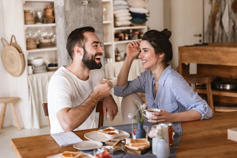 Pärchen sitzt lachend am Frühstückstisch und trinkt Kaffee