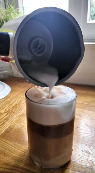 Milch wird aus einem MIlchaufschäumer in einen Latte Macchiato gegossen