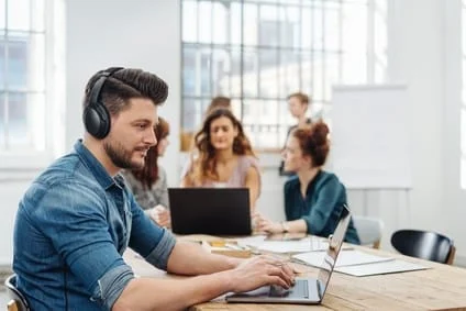 Mann im Büro arbeitet an Tisch mit Noisce-Cancelling-Kopfhörern